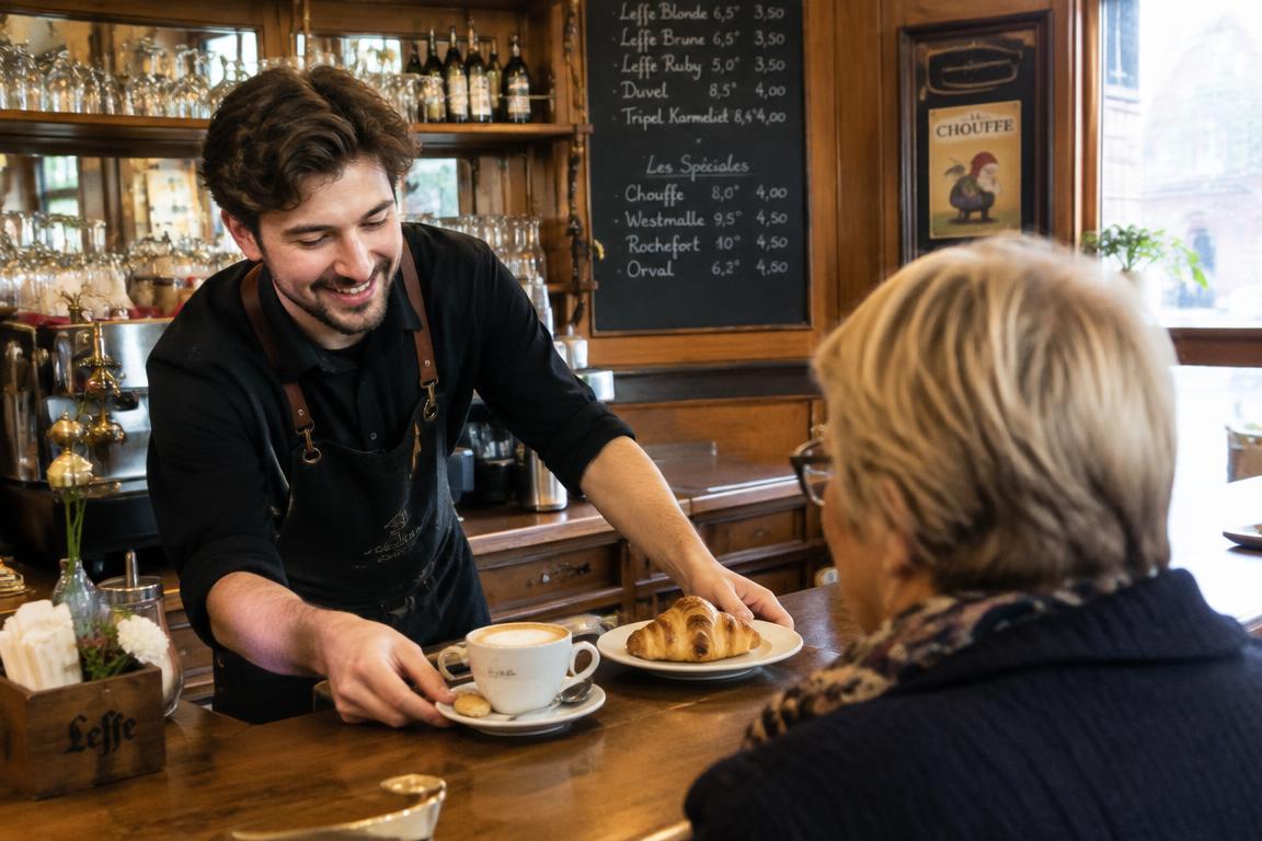 Serveur accueillant une cliente au comptoir d’un café